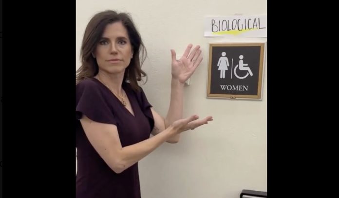 La republicana Nancy Mace colocando un cartel para indicar que los baños del Capitolio han de ser usados según el sexo biológico.