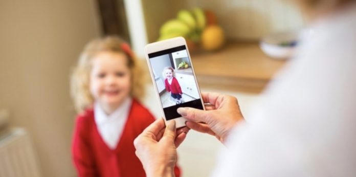 Imagen de una niña mientras es fotografiada con el móvil por una adulta.